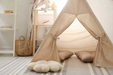 Stylish toy wigwam, furniture, pillows and decor near window in playroom. Interior design © New Africa