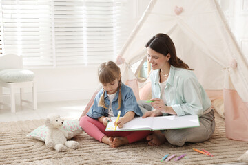 Mother and her daughter drawing in sketchbook together near toy wigwam at home, space for text © New Africa