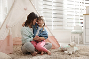 Mother and her daughter near toy wigwam at home, space for text © New Africa