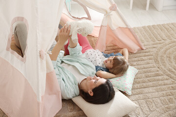 Mother and her daughter with toy near wigwam at home, above view © New Africa