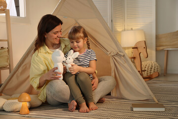 Mother and her daughter with toys near wigwam at home © New Africa