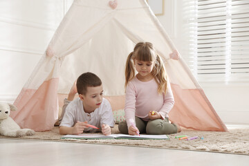Little kids drawing in sketchbook together near toy wigwam at home © New Africa