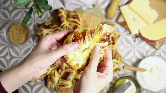 hand holding Delicious turkish ramadan Golden Braided Star Bread With Cheese, Butter sits on a patterned table, surrounded by cheese, flour, sesame seeds