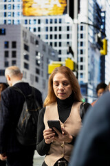Fototapeta premium Portrait of active businesswoman professional browsing apps on busy city avenue, surrounded by a multicultural crowd in motion and highlighting urban lifestyle. Realistic everyday city life.