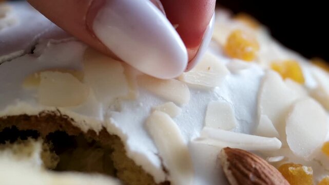 Macro breaking white icing on Easter kulich almond flakes and candied fruit close-up texture crust sweet bread detail