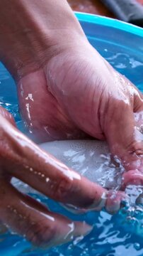 Squid cleaning and preparation by hand with ink release washing in blue basin and draining in yellow colander showing traditional Asian seafood process