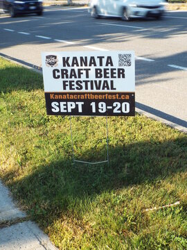 Gloucester, Ontario, Canada &ndash; July 24, 2025: A "Kanata Craft Beer Festival" lawn sign features a QR code, website, and event dates alongside a busy road on River Rd.