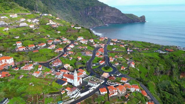 Aerial view of Arco da Faial, Madeira, a charming village nestled on a lush green mountainside. Traditional houses, a church, and winding roads define this picturesque coastal community.