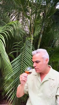 Hispanic Mature Man Tasting Aged Rum or Brandy in Tropical Garden 
