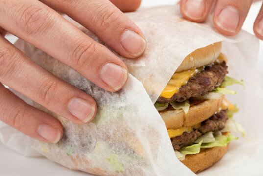 Hands carefully wrapping a large freshly made double cheeseburger in thin white greaseproof packaging paper