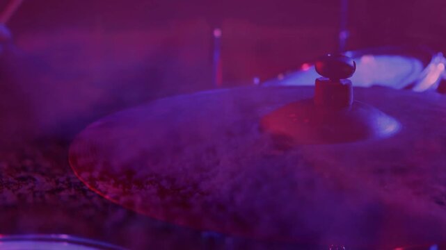 metallic drum cymbal glowing under pink stage lighting while smoke drifting across surface