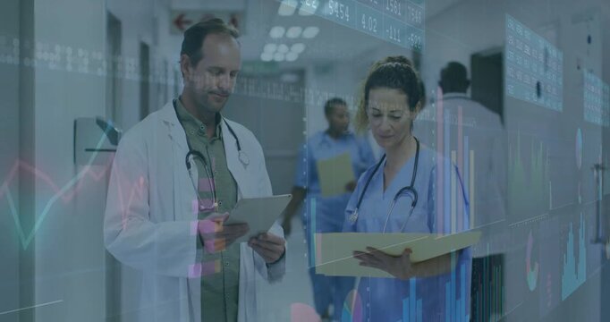 Doctor tapping tablet and overlaying graphs in medical corridor while nurse reviewing medical data