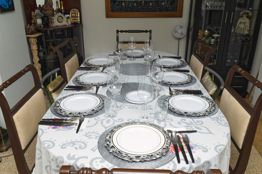 Elegant dining table set for eight with white tablecloth, silver chargers, glassware and cutlery arranged for formal meal at home