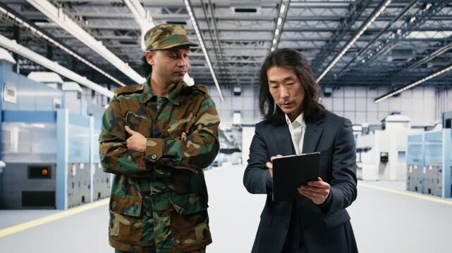 Soldier speaks with microchip production factory senior manager about using microelectronics for national security operation. Army officer and Asian man chat about semiconductor supply chain, camera B