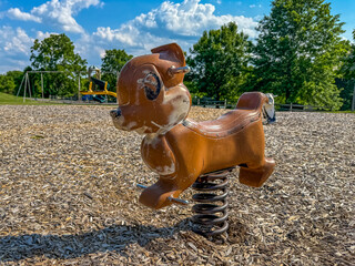 Old metal rocking chipmunk, squirrel, animal form, riding playground equipment for young children at a park, school, with chipped brown paint. 