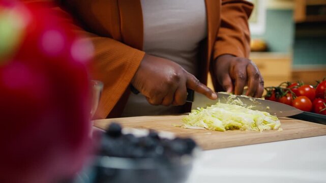 Black food blogger cutting iceberg salad on the cutting board, doing meal prep for a fresh salad bowl. Woman recording a culinary tutorial vlog at home kitchen, social media platforms.