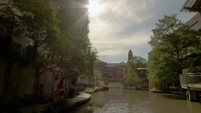 San Antonio Riverwalk with Tourists Strolling Along Path and Golden Sun Rays.