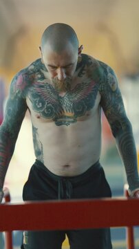 Tattooed muscular man doing dips on parallel bars