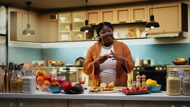 African american woman doing taste test for avocado on toast slices, good tasty breakfast idea rich in natural fats and proteins. Woman tasting the meal after making it, recording food vlog.