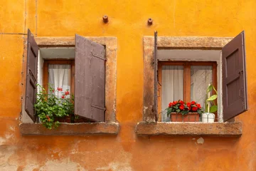 Two old windows with wooden shutters and flower pots on orange facade in Verona, Italy. © Kavalenkava