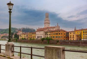 View of Verona across the Adige River with cathedral tower and historic riverside buildings, Italy. © Kavalenkava