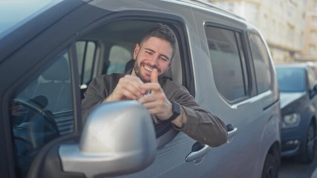Young man in driver's seat smiles while holding car keys and giving thumbs up through open window on a busy street; happiness trust.