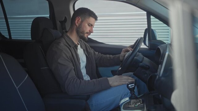 Man in car holds gearshift and leans forward inspecting the center console in building; contemplation.