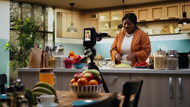 Food vlogger, african american, cutting salad leaves, for meal prep, recording video while she makes a fresh salad bowl recipe with vegetables. Culinary tutorial for online platforms, lifestyle.