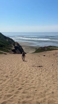Woman hiking down steep sandy path to the Pacific Ocean at Fort Funston (9:16 Vertical).