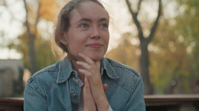 Happy grateful lady. Woman expressing happiness in outdoor setting. Woman seated outdoors smiling with hope and gratitude. Cheerful woman dressed in denim sharing joyful moments on park bench