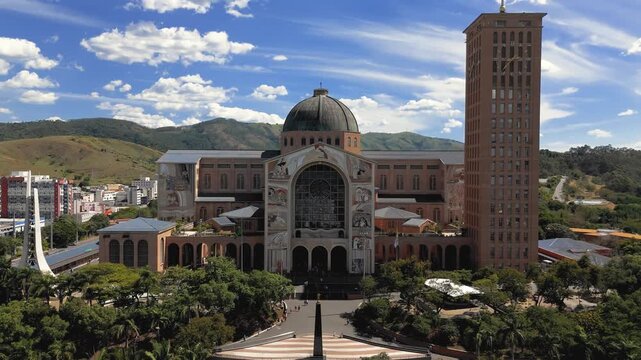 Aerial view of National Shrine basilica facade with tower, dome, religious murals and Brazilian and Vatican flags in Aparecida, Brazil. Push in camera movement