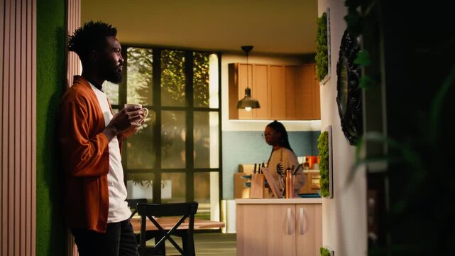 Black person serving a cup of coffee or tea at home on the weekend, relaxing and enjoying daylight in warm interior. Comfortable simple moment with hot drink, casual lifestyle.