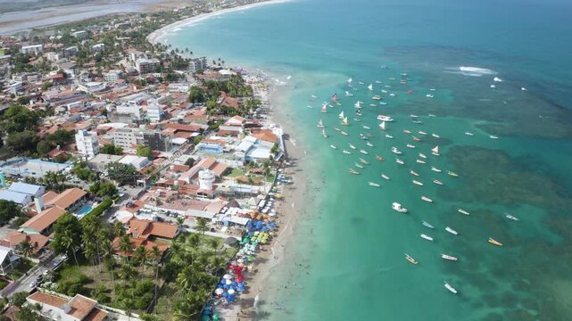 4K drone view of Porto de Galinhas beach, Brazil, with turquoise water, boats and coastal town, showing tropical landscape and tourism.