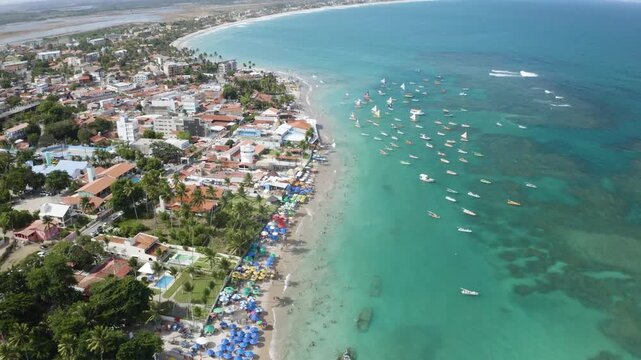 4K drone view of Porto de Galinhas beach, Brazil, with turquoise water, boats and coastal town, showing tropical landscape and tourism.