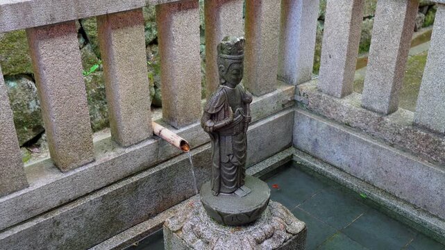 Kyoto, Japan - Oct 11 2025, 4k, Close-up view of a small bronze sculpture of a saint plased in a small stone pool, on the territory of Kiyomizu-dera Temple, without people, Kyoto, Japan