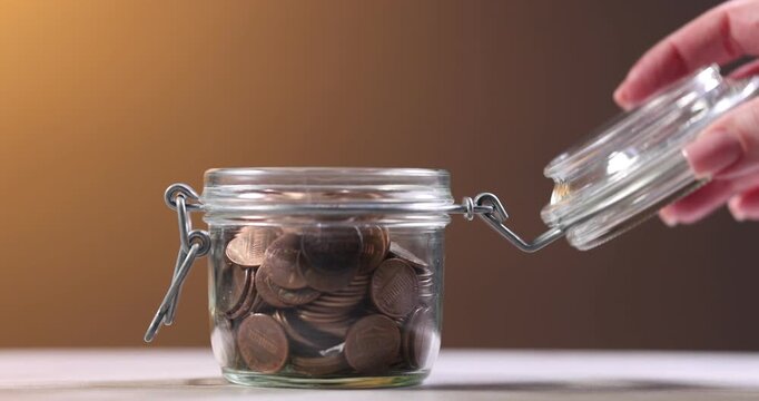 Woman putting coins into glass jar at white table, closeup