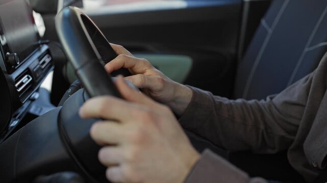 Man with bare hands on steering wheel, fingers tapping controls and touching wheel while driving on street in car interior; calm concentration.