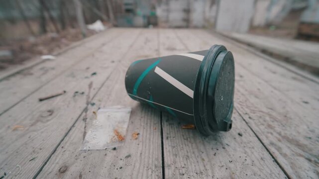 Ultra-Wide Close-up of Abandoned Paper Coffee Cup on Wooden Picnic Table | Disposable Takeaway Cup Littering in Nature | Concept of Environmental Pollution and Human Impact