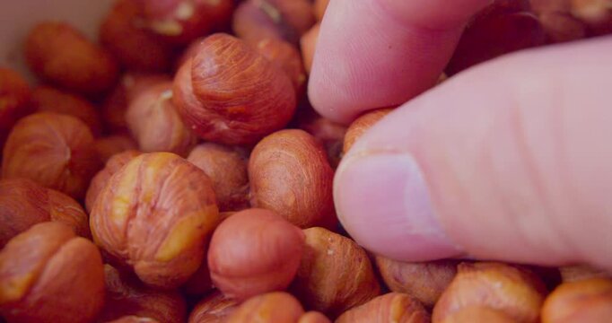 Close-up of fingers picking up peeled hazelnuts from a plate.