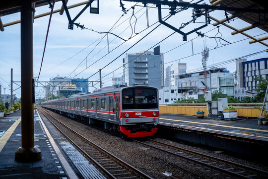 Jakarta, Indonesia - March 24, 2026: KAI Commuter train arriving at Gondangdia Station platform, framed by urban buildings and overhead power lines.