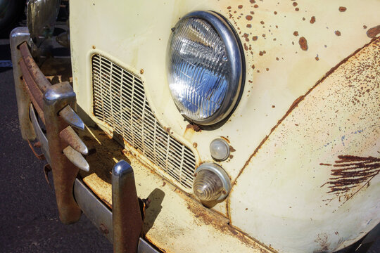 Front side of a vintage classic car with creamy yellow colored surfaces and shiny chrome-bezeled headlight glass and dull signal lights