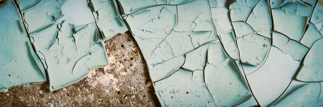 Peeling paint on the wall. Panorama of a concrete wall with old cracked flaking paint. Weathered rough painted surface with patterns of cracks and peeling. Wide panoramic grunge texture for background