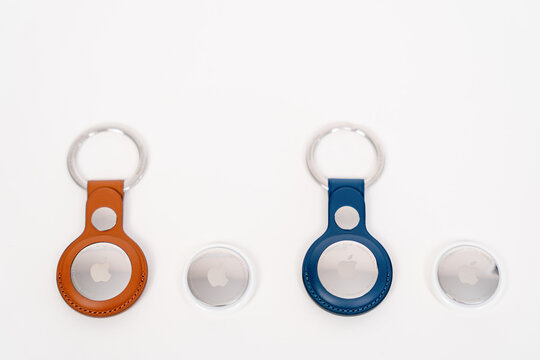 Rostov, Russia - April 04, 2022: Two Apple AirTag trackers with orange and blue keychain holders arranged on a white background alongside the round tracking devices in a clean product composition