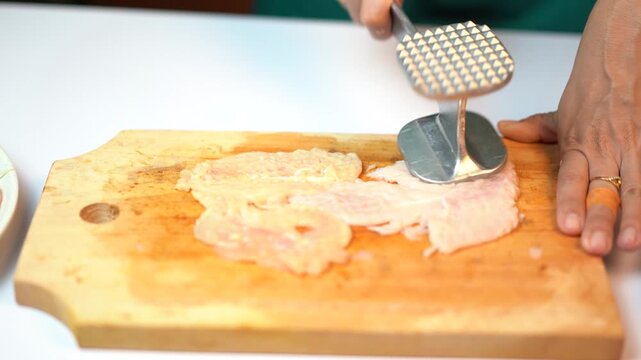 Tenderizing Raw Chicken Breast with Metal Meat Hammer on Wooden Board