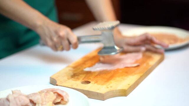 Woman Hand Tenderizing Raw Chicken Breast on Wooden Board