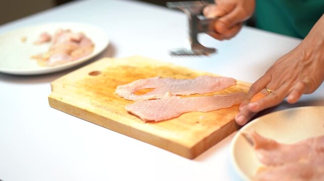 Chef Pounding Chicken Breast with Meat Mallet on Wooden Cutting Board