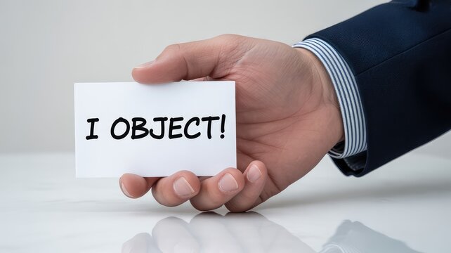 Close-up of a well-dressed hand holding a white card with the words "I OBJECT!" clearly printed, representing dissent or legal protest.