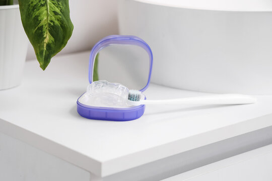 Box with occlusal splint and toothbrush near sink in bathroom, closeup