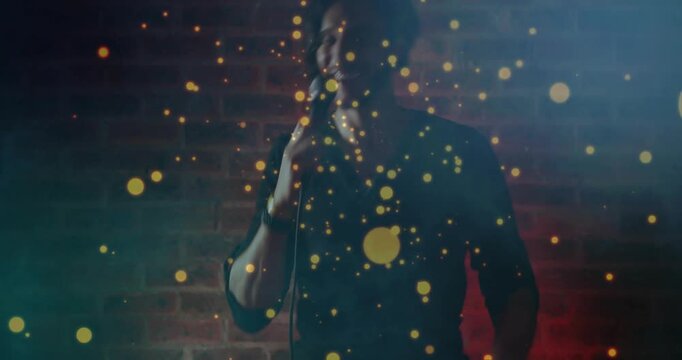 Male singer launching into song by brick wall with wired mic, gold particles drifting across face