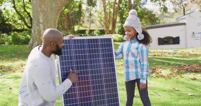 Man kneeling pointing at solar panel cells while child supporting panel, learning solar technology